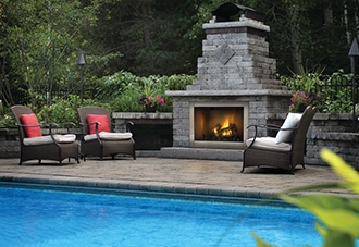 Outdoor fireplace next to two chairs and a pool.